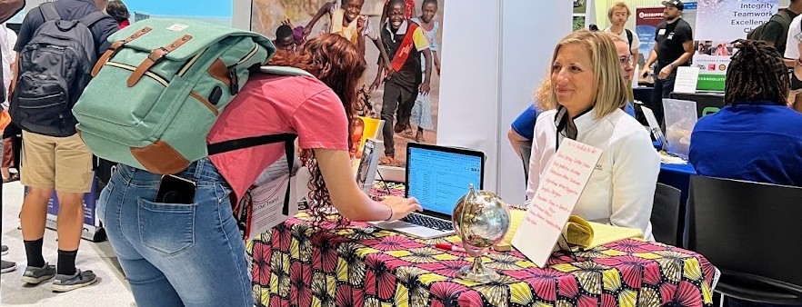 A co-op employer sits behind a table smiling while a student fills out a form on a laptop